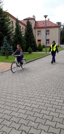 Dziecko na rowerku na placu szkolnym za nim policjant