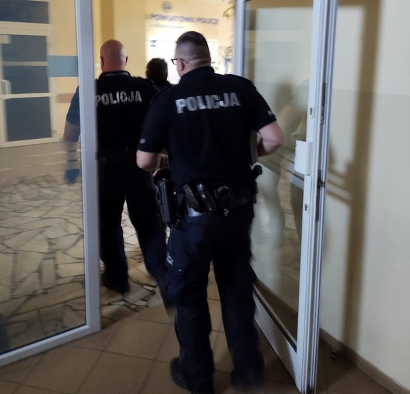 Policjanci przeprowadzający zatrzymanego przez kraty aresztu