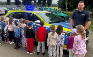Grupa dzieci oglądająca radiowóz oraz policjant