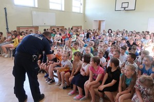 Sala gimnastyczna wypełniona dziećmi i pochylający się do nich policjant