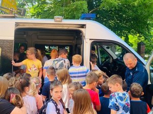 Grupa dzieci i policjant t oglądający radiowóz typu bus