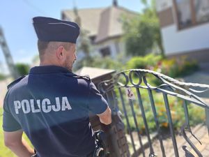 Policjant widziany od tyłu przy furtce wejściowej na posesję