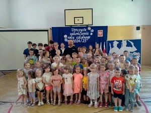 Na sali gimnastycznej pozująca do zdjęcia z policjantem grupa dzieci
