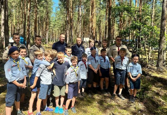 Grupa harcerzy praz dwóch policjantów pozująca do zdjęcia w kompleksie leśnym