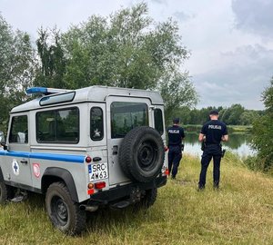 Terenowy samochód nad brzegiem zbiornika wodnego oraz dwaj policjanci