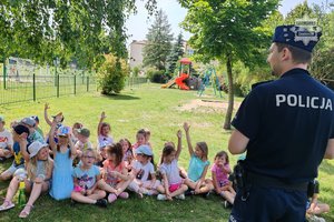 Policjant prowadzący pogadankę dla grupki dzieci siedzącej na trawie
