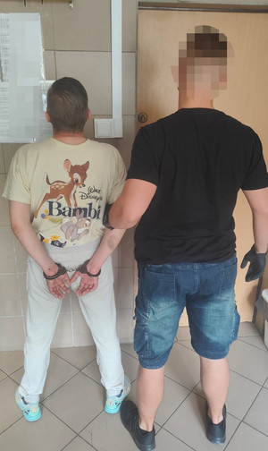 Mężczyzna przytrzymujący drugiego mężczyznę ze skutymi kajdankami rękoma przy ścianie