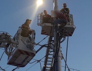 Policjanci wraz ze strażakami na podnośnikach pomagają mężczyźnie siedzącemu na słupie energetycznym