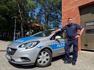 Umundurowany Policjant stojący przy oznakowanym radiowozie