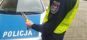 Policjant z alkomatem na tle radiowozu