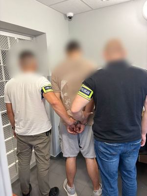 Nieumundurowani policjanci trzymają zakutego w kajdanki  mężczyznę