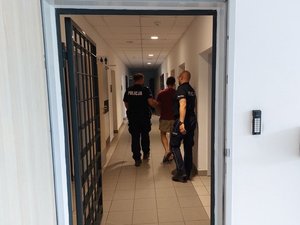 Umundurowani policjanci w pomieszczeniu prowadzą zatrzymanego mężczyznę