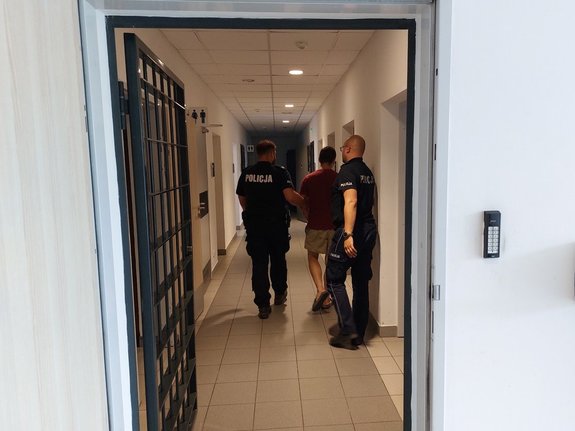 Umundurowani policjanci w pomieszczeniu prowadzą zatrzymanego mężczyznę