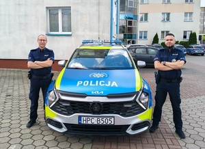 Dwóch umundurowanych policjantów stoi przy radiowozie