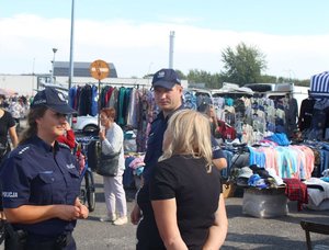 Dwójka policjantów oraz kobieta na tle targowiska miejskiego