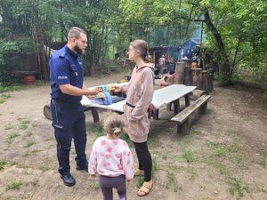 Policjant oraz kobieta i dziecko na tle leśnego obozu