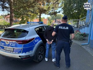 Policjant wprowadzający zatrzymanego i skutego kajdankami mężczyznę do radiowozu