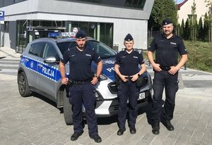 Trójka policjantów na tle radiowozu i komisariatu