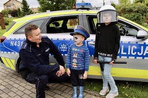 Dwójka dzieci na tle radiowozu obok kucający policjant