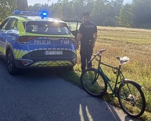 Na polnej jezdni na pierwszym planie rower, dalej radiowóz i policjant