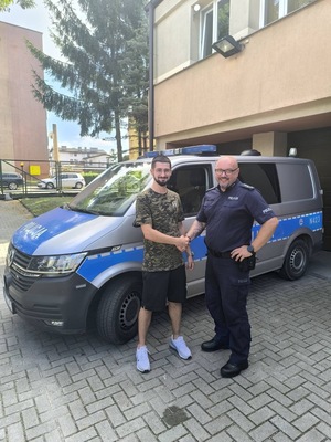 Na tle radiowozu młody mężczyzna ściskający dłoń policjantowi
