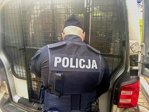 Widziany od tyłu policjant zamykający kratę przedziału dla zatrzymanych radiowozu