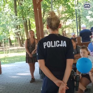 Widziana od tyłu policjantka prowadząca pogadankę dla dzieci zgromadzonych pod altaną
