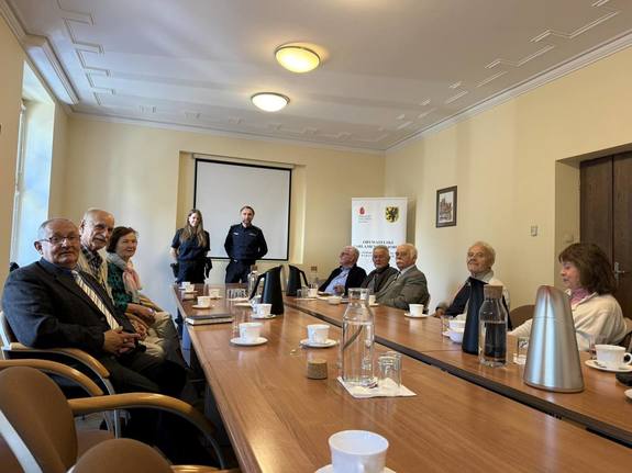 Dwójka policjantów oraz seniorzy siedzący przy stołach konferencyjnych