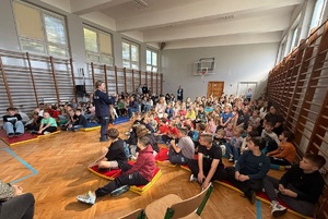 Policjantka prowadząca prelekcję dla siedzących w sali gimnastycznej grupy dzieci
