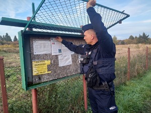 Policjant wieszający ulotkę na tablicy ogłoszeń w odkrytym terenie