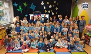 Policjant z wychowawczyniami i dużą grupą przedszkolaków pozujący do zdjęcia w sali