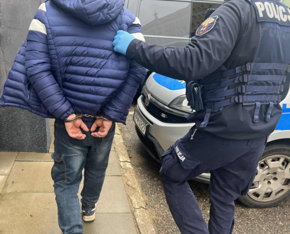 Zbliżenie widzianych z tyłu: policjanta przytrzymującego skutego kajdankami z tyłu mężczyznę