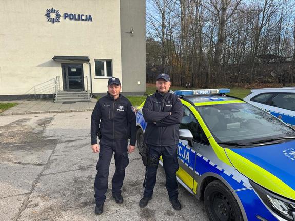 Umundurowani policjanci przy radiowozie w tle budynek komendy