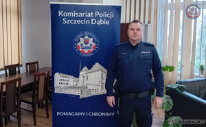 Policjant stojący wewnątrz pomieszczenia obok banneru Komisariatu Policji Szczecin Dąbie