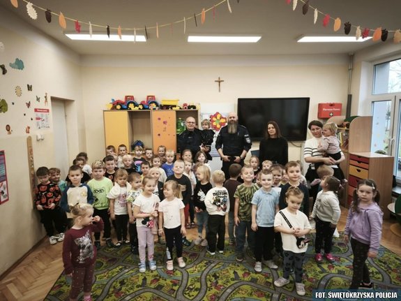 Dwaj policjanci, dwie wychowawczynie oraz grupa dzieci pozująca do zdjęcia w sali szkolnej