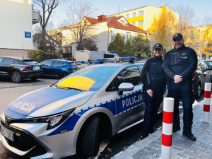 Dwójka policjantów na tle radiowozu i osiedla mieszkaniowego