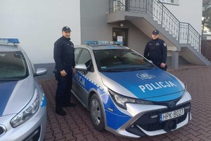 Dwaj policjanci przy radiowozie na tle komisariatu