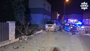 W scenerii nocnej dwa rozbite samochody oraz zniszczony płot posesji