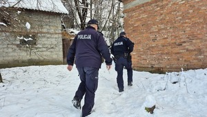 W scenerii zimowej dwaj policjanci idący w kierunku zrujnowanego budynku