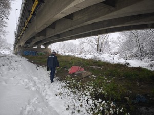W scenerii zimowej policjant pod wiaduktem drogowym, na ziemi widoczna kołdra
