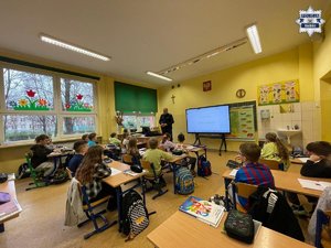 Policjant prowadzący pogadankę w sali szkolnej wypełnionej uczniami siedzącymi w ławkach