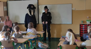 Policjantka oraz maskotka policyjna w kształcie borsuka podczas pogadanki w sali szkolnej