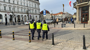 Trójka policjantów widziana z tyłu na ulicy warszawskiej Starówki