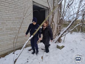 W scenerii zimowej policjantka oraz kobieta w kurtce idące wzdłuż ściany pustostanu