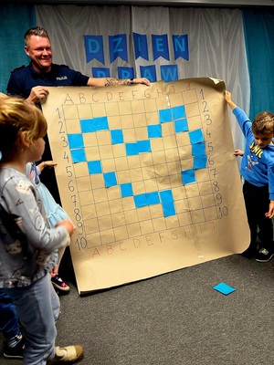 Policjant wraz z dwójką dzieci trzymający dużą planszę z narysowanym niebieskim sercem