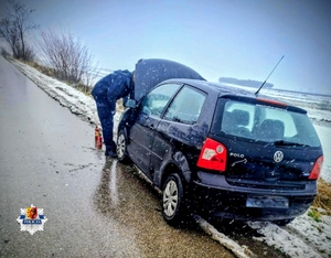 Pochylony pod maską silnika samochodu stojącego na poboczu drogi mężczyna