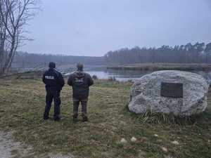 Nad brzegiem zbiornika wodnego widziani z tyłu policjant i strażnik leśny