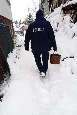 Widziany od tyłu policjant z wiadrem idący w śniegu między dwoma budynkami