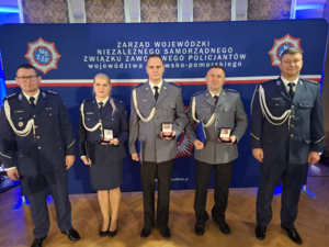 Piątka policjantów pozująca do zdjęcia, trójka z nich trzyma w rękach pudełeczka z odznakami