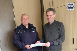 Uśmiechnięci policjant i mężczyzna w swetrze przekazujący sobie plik dokumentów.